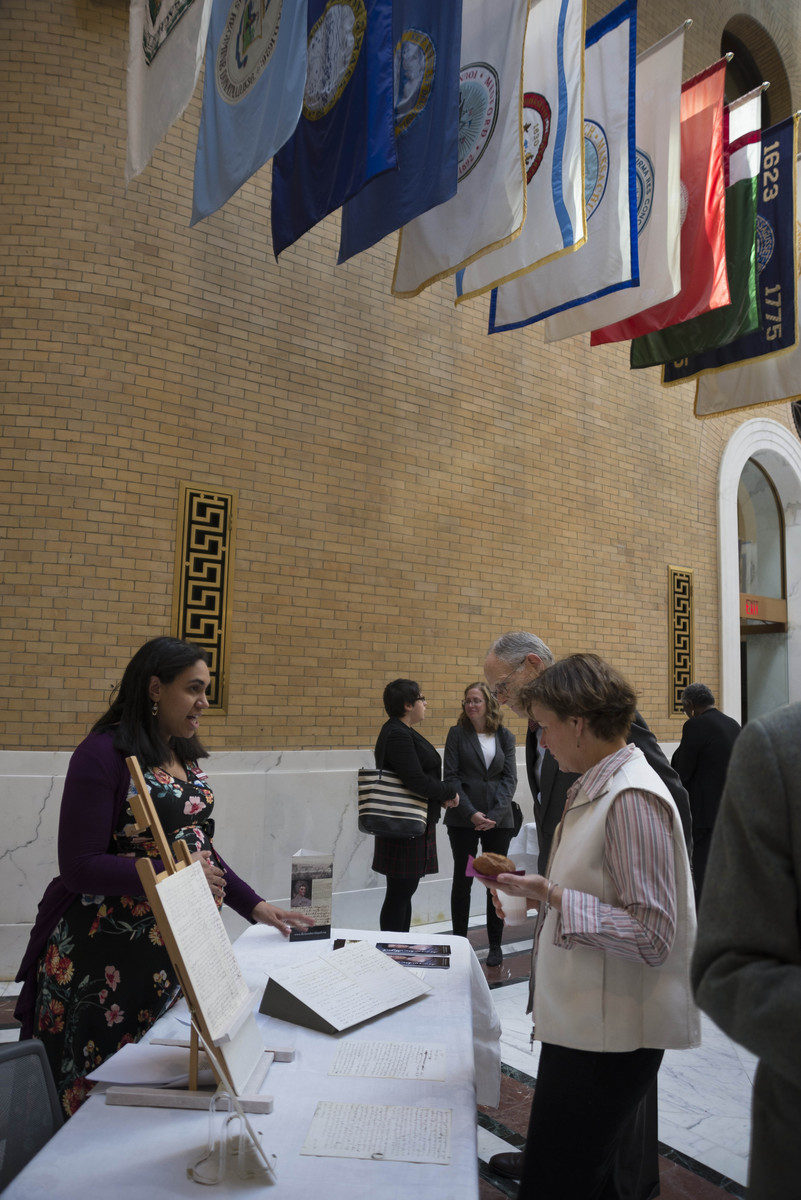 Woman standing behind table speaking to man and woman on other side in government building